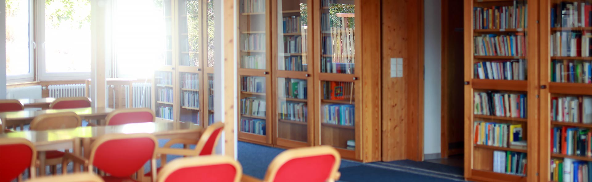 OJC Begegnen – Seminarraum mit Bücherregalen aus hellem Holz, Glastüren zum Schutz der Bücher und Roter Bestuhlung.